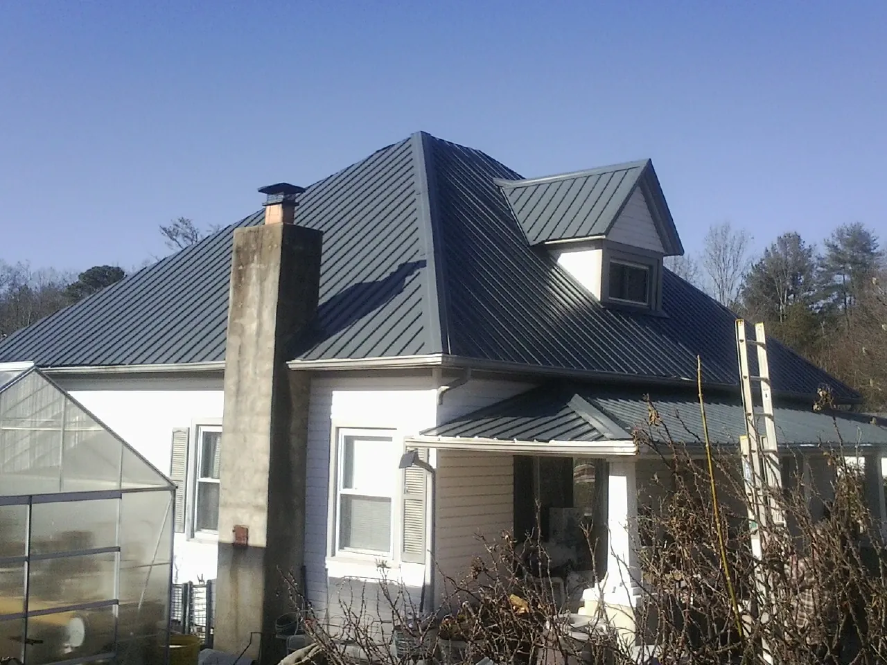 Dark blue standing seam metal roof on a white farmhouse with dormer — Slate & Tile Roof Repair by Roofing Brothers in Earling