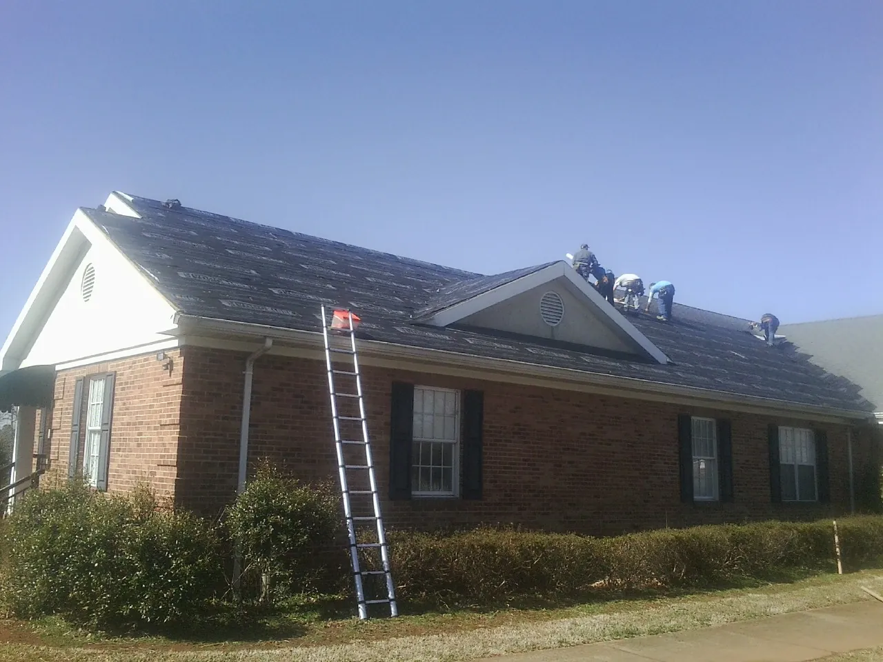 Crew tearing shingles off a brick ranch roof with a ladder set — Emergency Roof Repair work by our crew in Earling