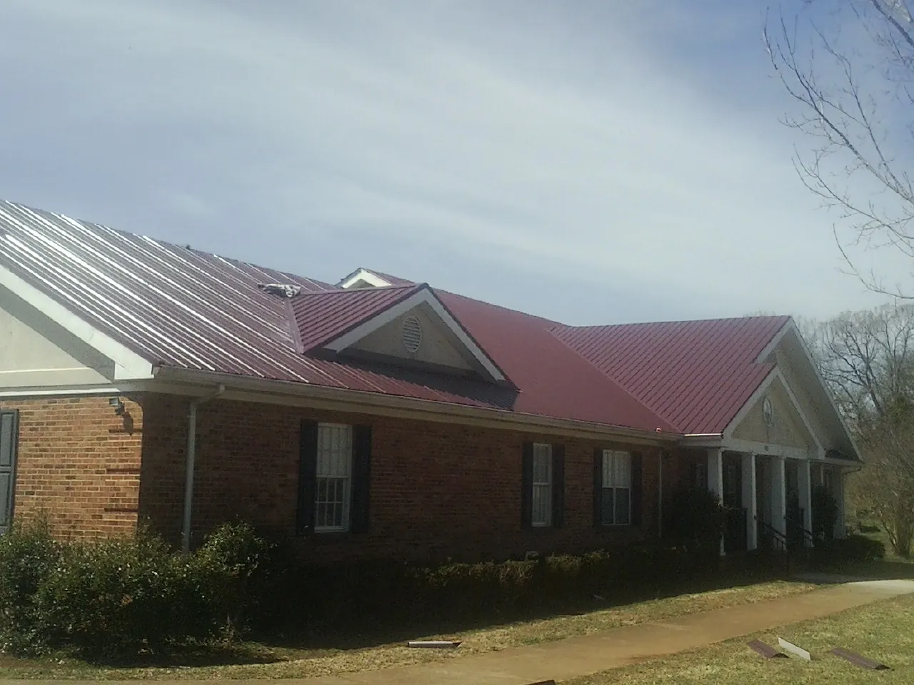 Red metal roof with gabled entries on a long brick building, from a Hail Damage Roof Repair job in Earling