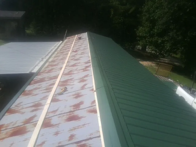 Old rusted panels beside newly installed green metal roofing — Wind Damage Roof Repair by Roofing Brothers in Earling