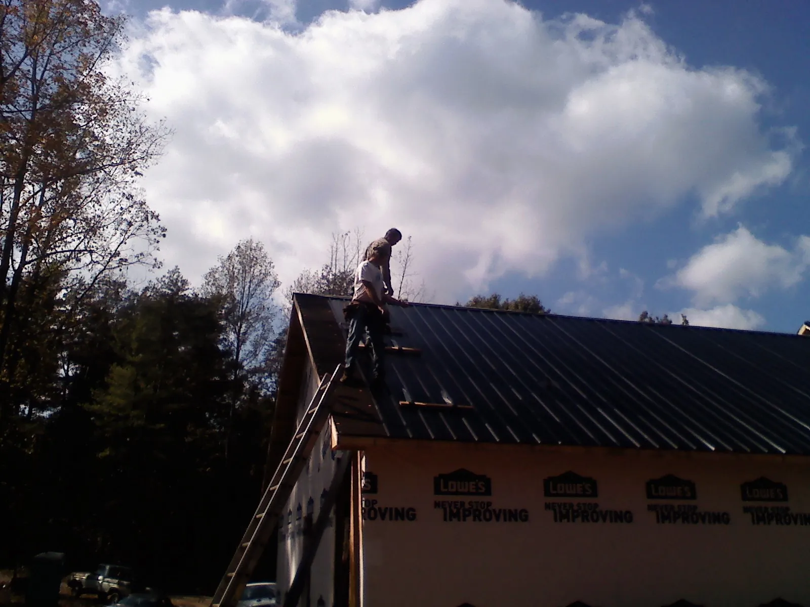 Roofer fastening dark metal panels high against a cloudy sky, from a Roof Inspection job in Earling