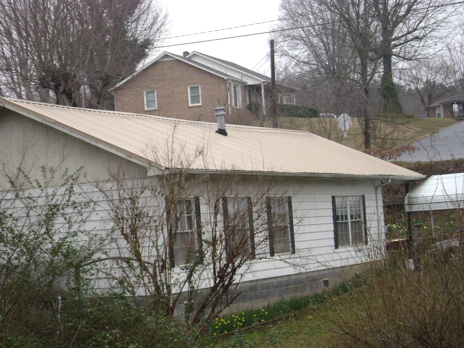 Tan metal roof on a white sided house set into a hillside — Commercial Roofing by Roofing Brothers in Earling