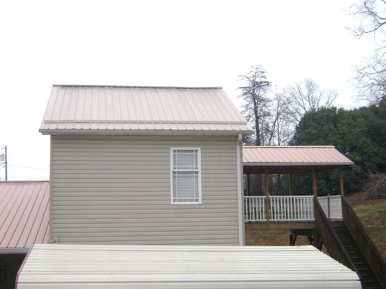 Tan metal roofs on a two story addition and attached porch, from a Roof Replacement job in Earling